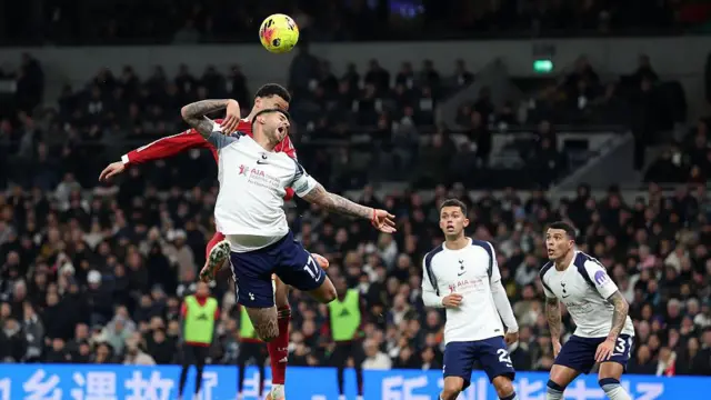 Hugo Ekitike heads the ball in a challenge with Cristian  Romero
