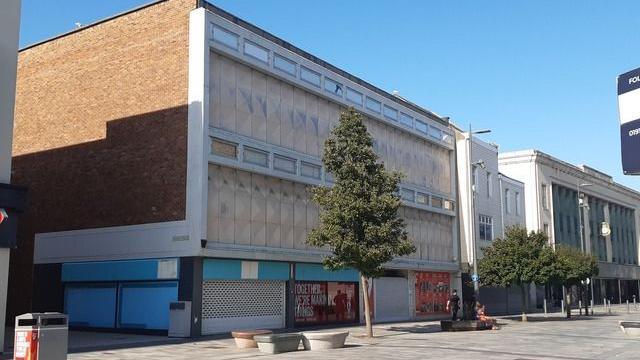 A row of boarded up shops with a pedestrianised street in front of them. 