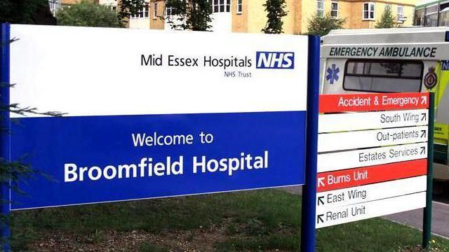 A sign at the entrance of Broomfield Hospital. It says "Welcome to Broomfield Hospital". To the right of it is another sign giving directions to the various units. There is an ambulance in the background, to the right. 