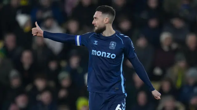Matt Grimes holding his thumb up in a dark blue away kit during Coventry City's game against Norwich City