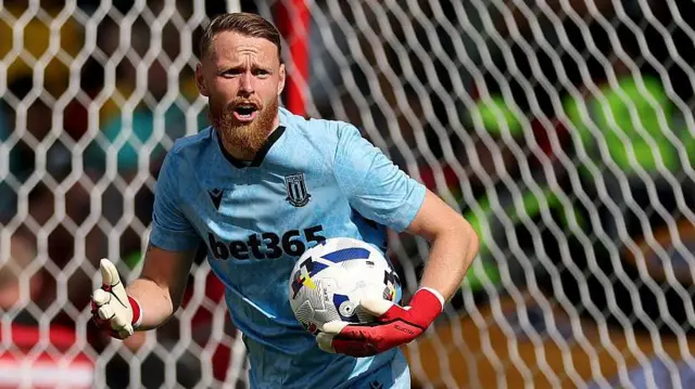 Stoke City goalkeeper Viktor Johansson in his blue shirt holding the ball in his left hand as he prepares to restart the play