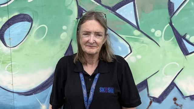 Director of Sk8side Deirdre O'Neill stands in front of a graffiti wall that says Sk8side