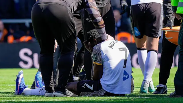 An image of Patrick Agyemang sitting on a football field surrounded by medics with his hands across his face in disappointment after picking up an injury