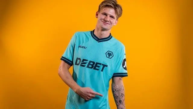 David Moller Wolfe points to wolf tattoo on his arm while wearing Wolves away shirt