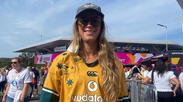 A woman wearing a yellow and green Australia rugby shirt along with a grey hat and sun glasses.