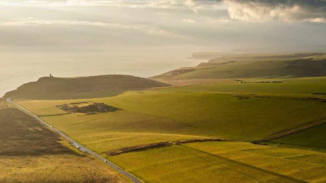 An ariel view of a road. fields in either side of the road. grey clouds in the sky.