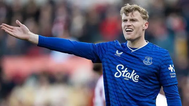 Jarrad Branthwaite in a blue Everton top, shouting and holding his arm out to the left