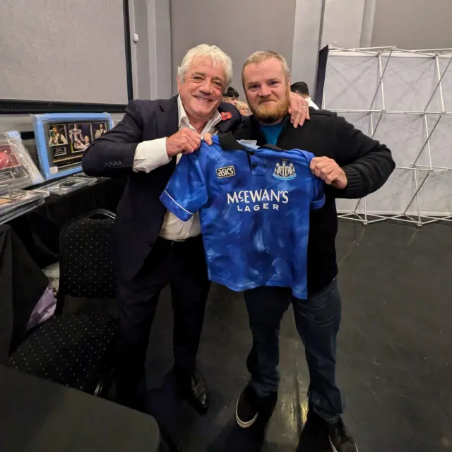 A man holds signed Newcastle blue 1993-94 away kit alongside Kevin Keegan