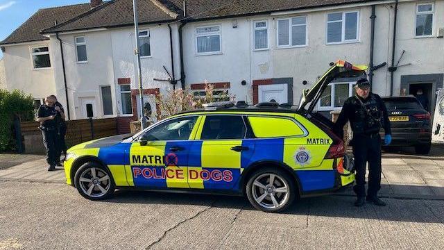 Police officers and police dogs car outside a house