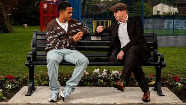 Fabio Carvalho and Michael Caulfield sitting together and talking on a bench, with a park and a play area in the background