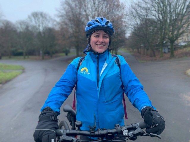 Sunny Cycles' Carol Thompson smiles on her bike in a rainy Kelvingrove park - but her bright blue helmet and jacket brighten up the picture. Four paths heading in different directions stretch out behind her.