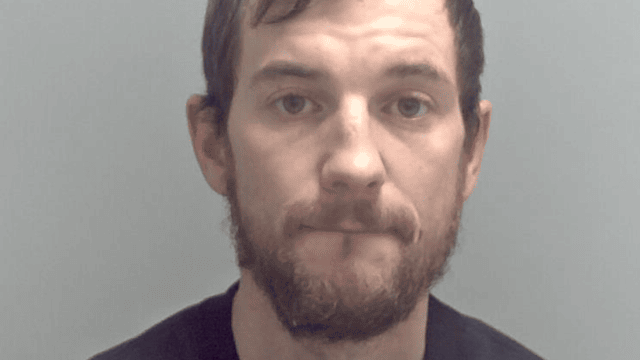 Kurtis Harper is pictured against a plain grey background. He has brown short hair and a beard.
