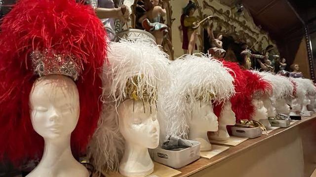 A row of nine or so foam heads. Some with red and silver feather head pieces on and the others white and gold feather head pieces.