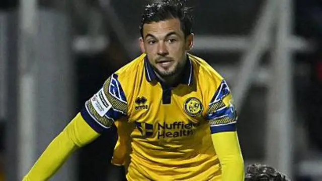 Jake Forster-Caskey in yellow Woking away shirt playing in a night match