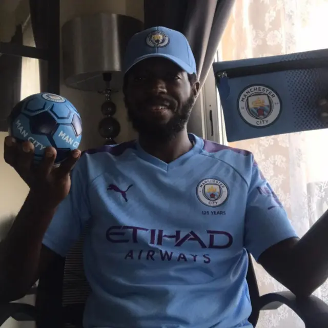 An image of a man holding up a mini Manchester City football and a Manchester City purse