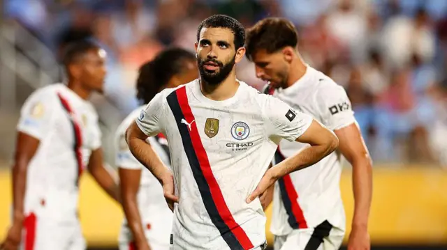 Rayan Ait-Nouri stands with his hands on his hips in Manchester City's away kit