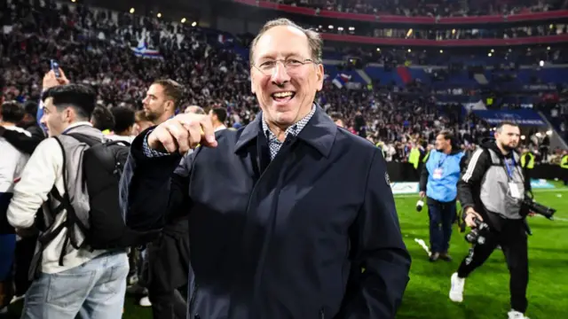 John Textor smiles while standing on a football pitch