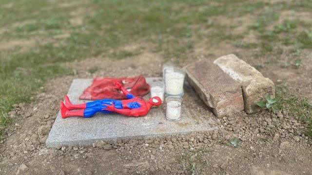 A paving stone with a Spider Man action figure on it and a couple of white candles.