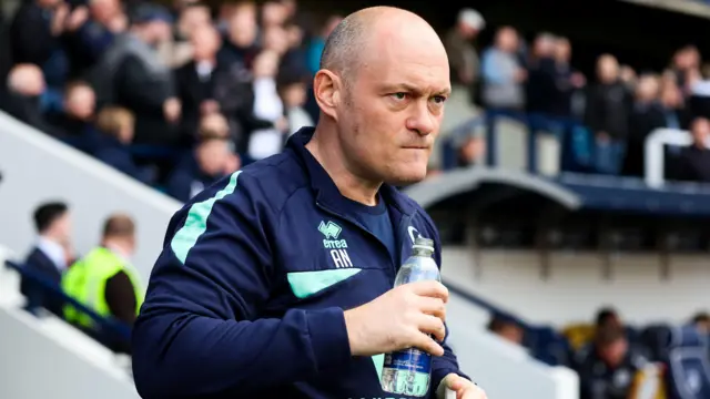 Alex Neil drinks from a bottle of water and looks focused on the Millwall touchline