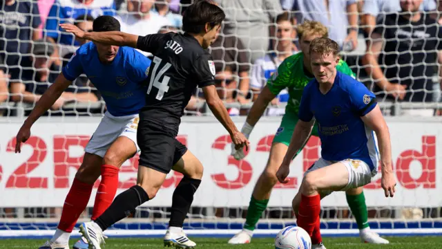 Koki Saito, wearing QPR's black away kit, moments before shooting to score against Portsmouth. The Portsmouth defenders, wearing their blue, white and red home kit can be seen trying to block his effort.