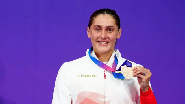Imogen Clark holds up her bronze medal in front of a purple background at the Commonwealth Games in Glasgow