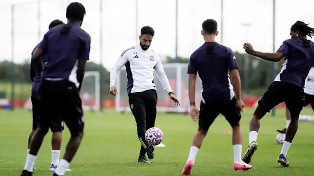 Ruben Amorim kicking a football during Manchester United training. There are four players with their backs to the camerea.