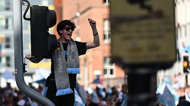 Manchester City fan hangs from a traffic light at the celebration parade