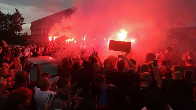 A flare burns red in a crowd of Crystal Palace fans outside Selhurst Park