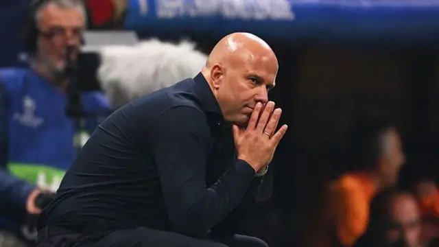 Arne Slot crouches and looks on thoughtfully during Champions League match