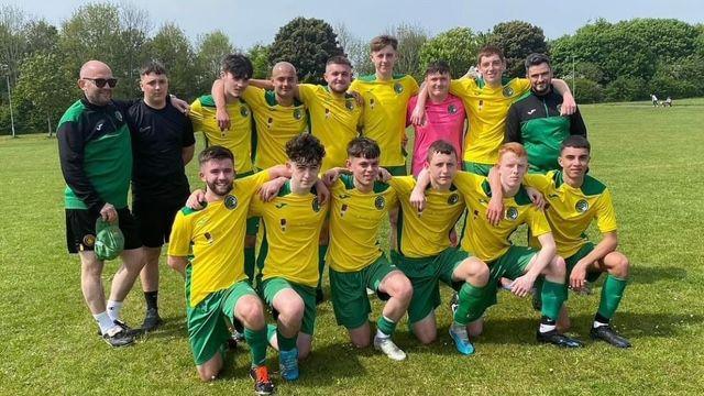 Two rows of young men in yellow football shirts with green shorts pose for a picture. The front row are kneeling down and the back row are standing