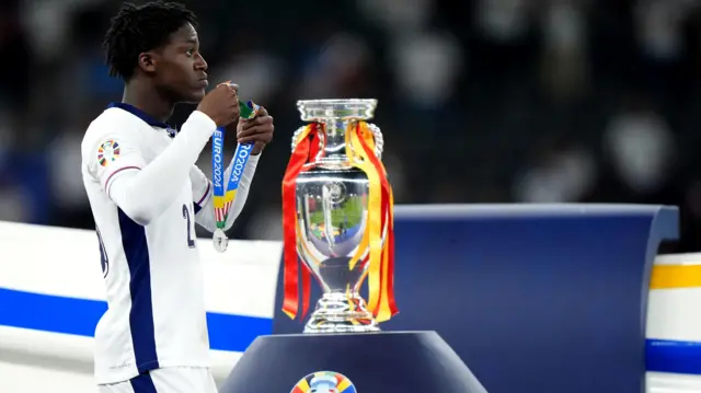 Kobbie Mainoo walks past the Euro 2024 trophy