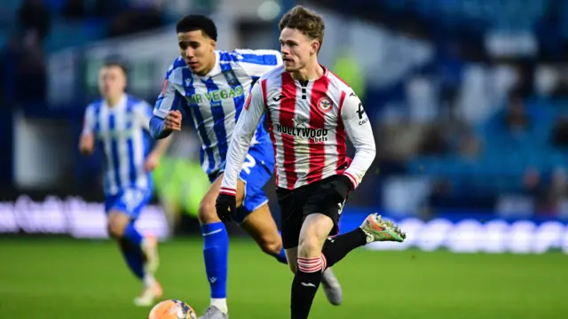 Brentford's Keane Lewis-Potter in red and white stripes runs clear of a Sheffield Wednesday defender in blue and white stripes