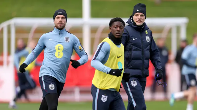 Thomas Tuchel, Head Coach of England, looks on as Jordan Henderson and Kobbie Mainoo of England run during a training session at St Georges Park