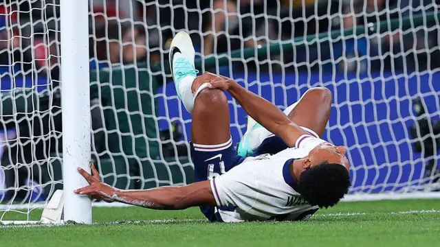 Ollie Watkins lying on the ground and holding his leg in pain after colliding with a goal post during England's match against Wales