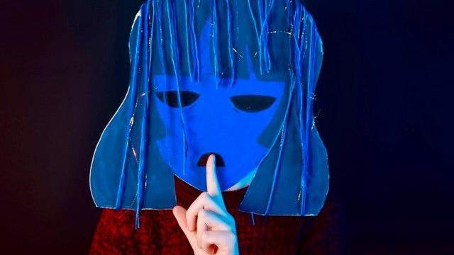 A bright blue face mask, with a person behind holding their finger to their lips