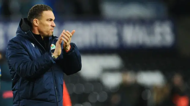 Valerien Ismael applauds fans while wearing a navy puffer jacket and a silver watch