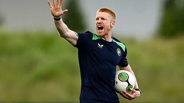 Paul McShane wearing a navy blue Republic of Ireland training top waves and shouts instructions during a training session