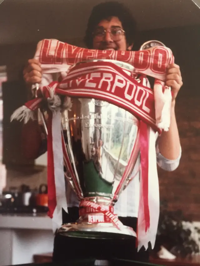A man clutches the European Cup with it draped in Liverpool scarves