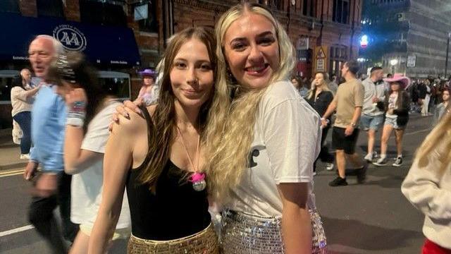 Two young women hugging in a crowd on the street