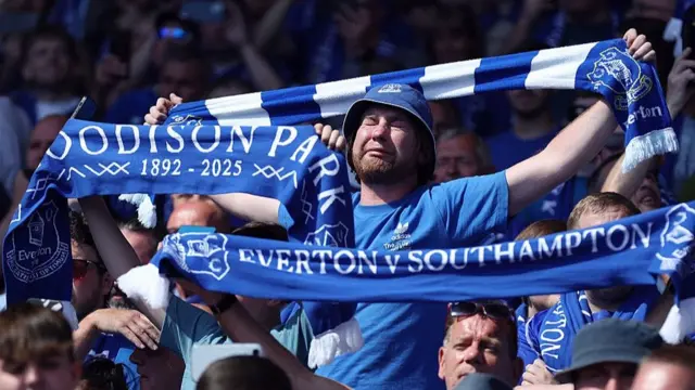 An Everton fan cries whilst holding a scarf in the crowd 
