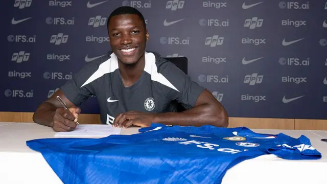 Moises Caicedo smiles and signs a Chelsea shirt