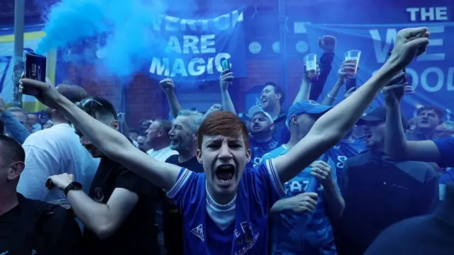 A young fan cheers whilst a flag displays 'Everton are Magic' 