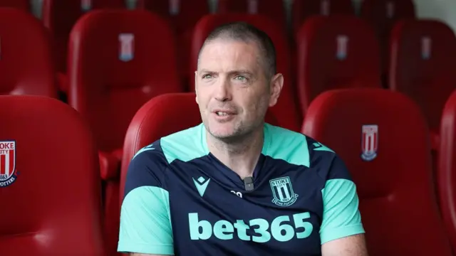 Gareth Owen sits in red seats with the Stoke City club badge on the headrests wearing his club training top