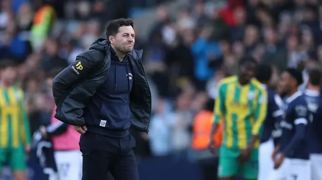 West Brom manager Ryan Mason adjusts the back of his sweatshirt and stares thoughtfully into middle distance after defeat