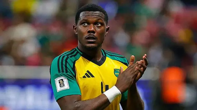 Ephron Mason-Clark in a yellow and green Jamaica shirt applauds supporters after their win over New Caledonia