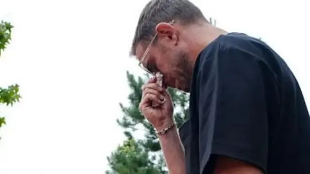 Jordan Henderson, wearing a black T-shirt and sunglasses, is tearful as he looks at tributes to Diogo Jota around Anfield