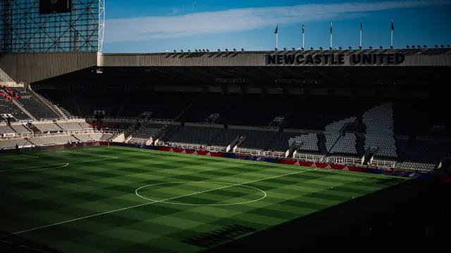 Half of an empty St James' Park taken from the opposite stand, with shadows of the stadium being cast over the pitch