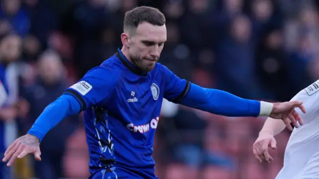 Liam Hogan stretches out his arms for balance as he clears a ball for Rochdale