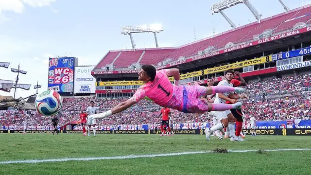 Max Crocombe, wearing New Zealand's pink goalkeeping kit and white gloves, dives in an attempt to stop Harry Kane's header during the friendly on 6 June