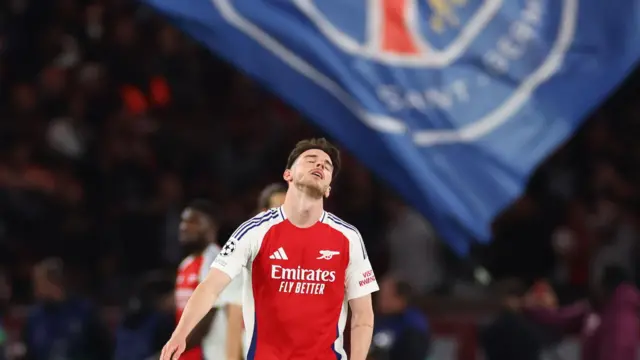 Declan Rice looks up dejectedly in front of PSG flag
